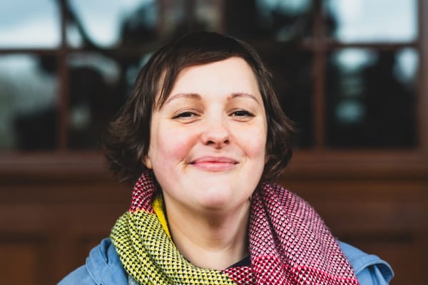 A women in a blue coat and colourful scarf smiles at the camera